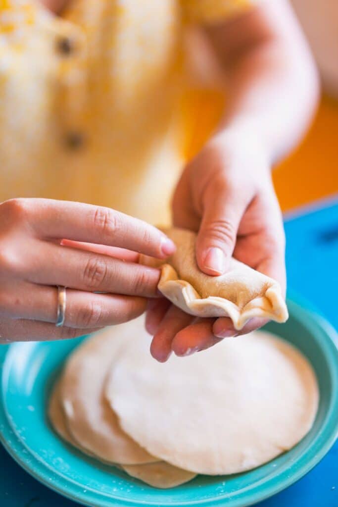 Hands carefully crafting homemade empanadas, showcasing traditional food preparation in a vibrant setting.